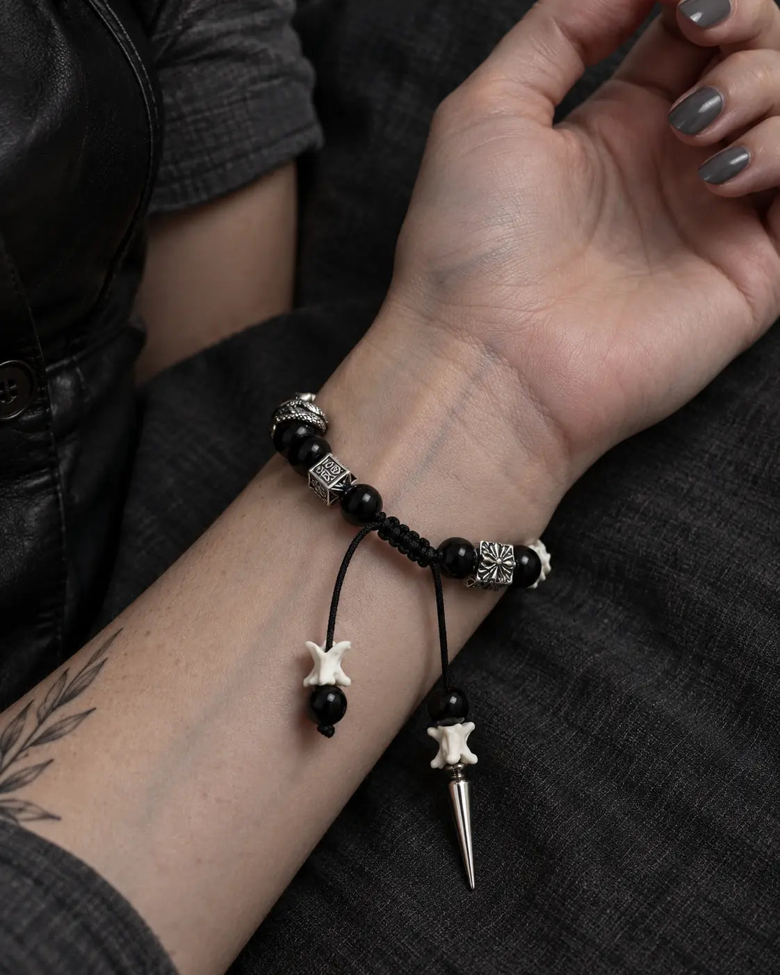 Palm-up view of the Obsidian Fang snake bone bracelet showing its braided knot and two hanging bone-tipped cords