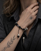 Obsidian Fang snake bone bracelet worn with the hand near the neck, showing its black beads and pointed drop