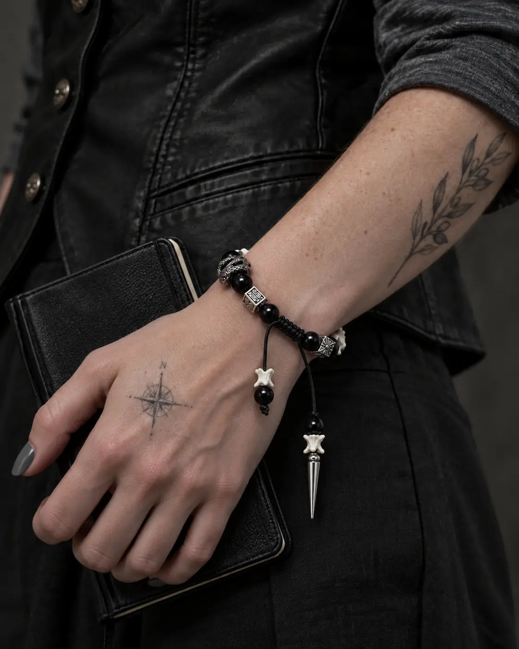 Obsidian Fang snake bone bracelet worn while holding a black book against a dark vest