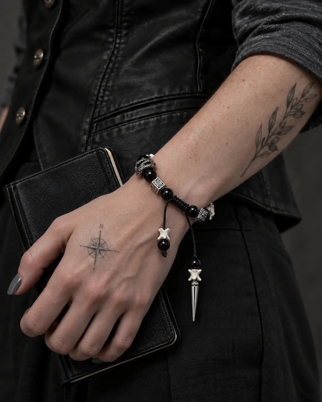 Obsidian Fang snake bone bracelet worn while holding a black book against a dark vest