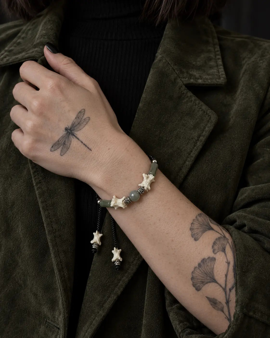 Olive Bead snake bone bracelet worn with the hand holding an olive jacket lapel
