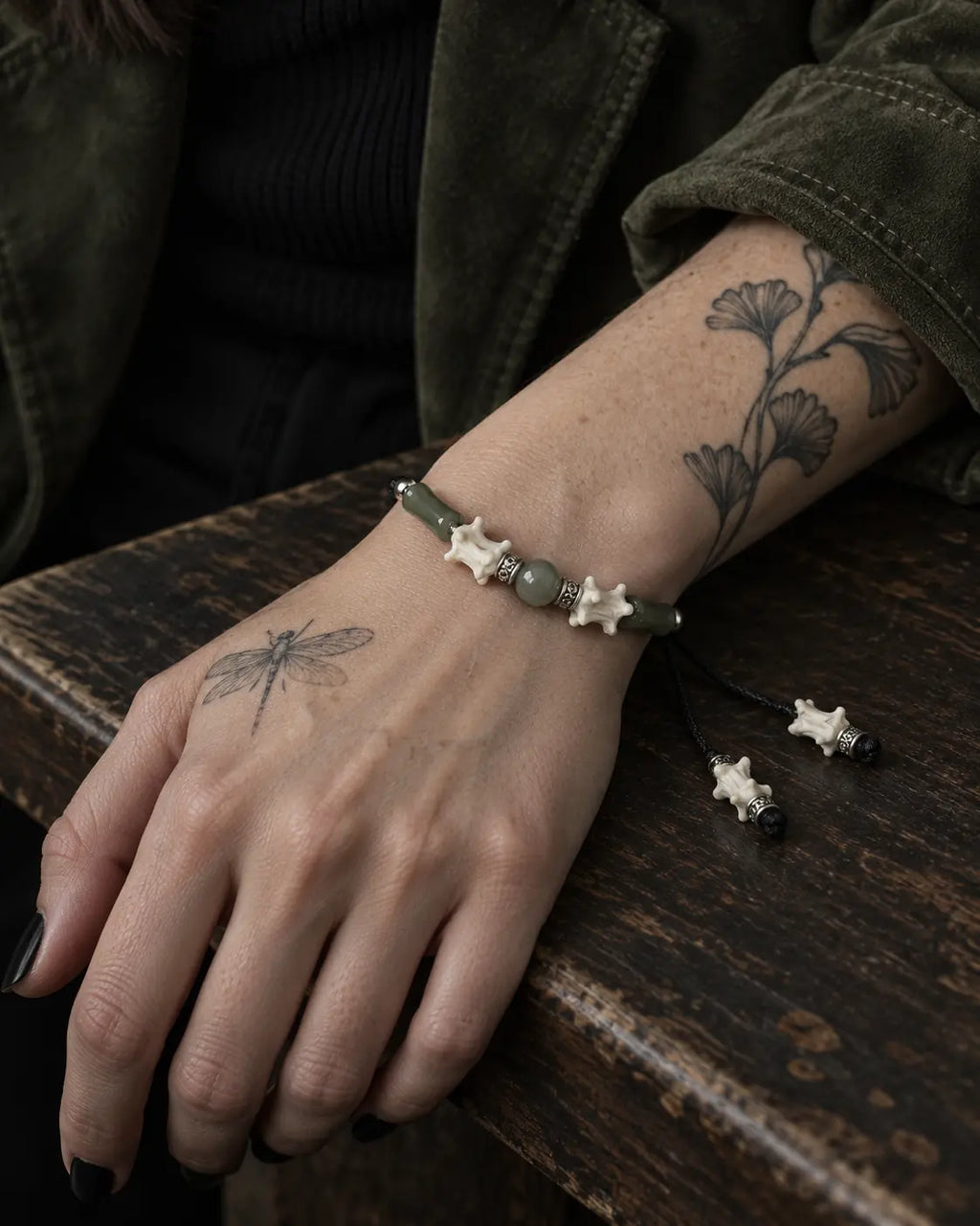Olive Bead snake bone bracelet on a wrist resting on a worn wooden table, with bone-tipped cords alongside
