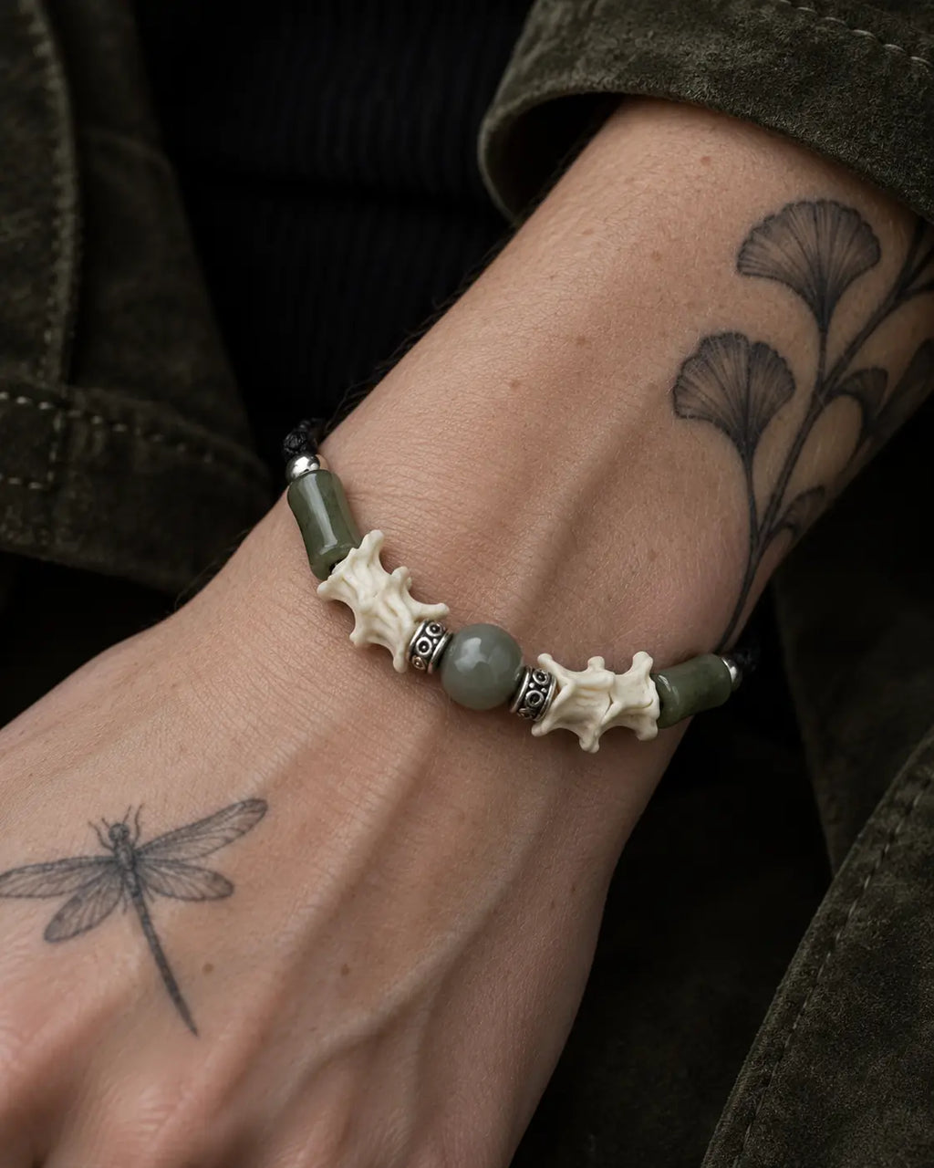 Close-up of the Olive Bead snake bone bracelet showing green beads, white vertebrae and engraved spacers on the wrist