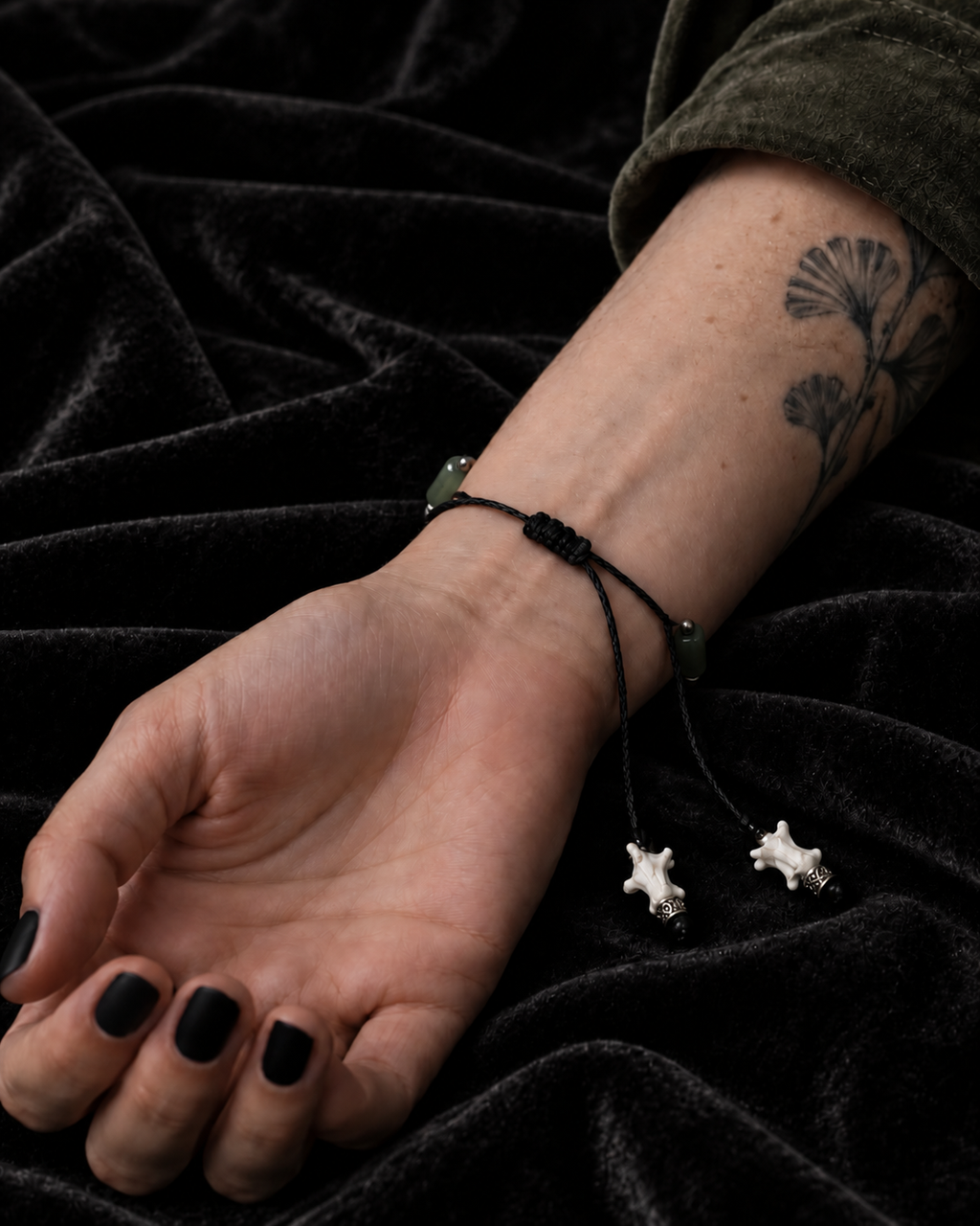 Palm-up view of the Olive Bead snake bone bracelet showing its black sliding knot and two white bone cord tips