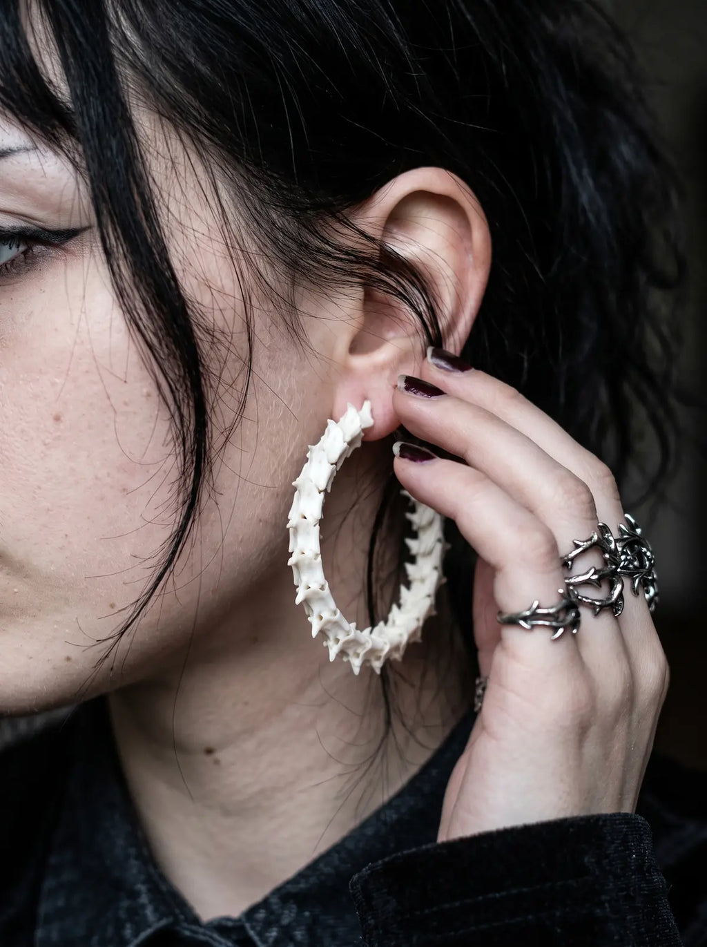 Ossuary Hoop snake bone earring worn with a ringed hand resting beside the ear