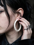 Ossuary Hoop snake bone earring worn with a ringed hand resting beside the ear