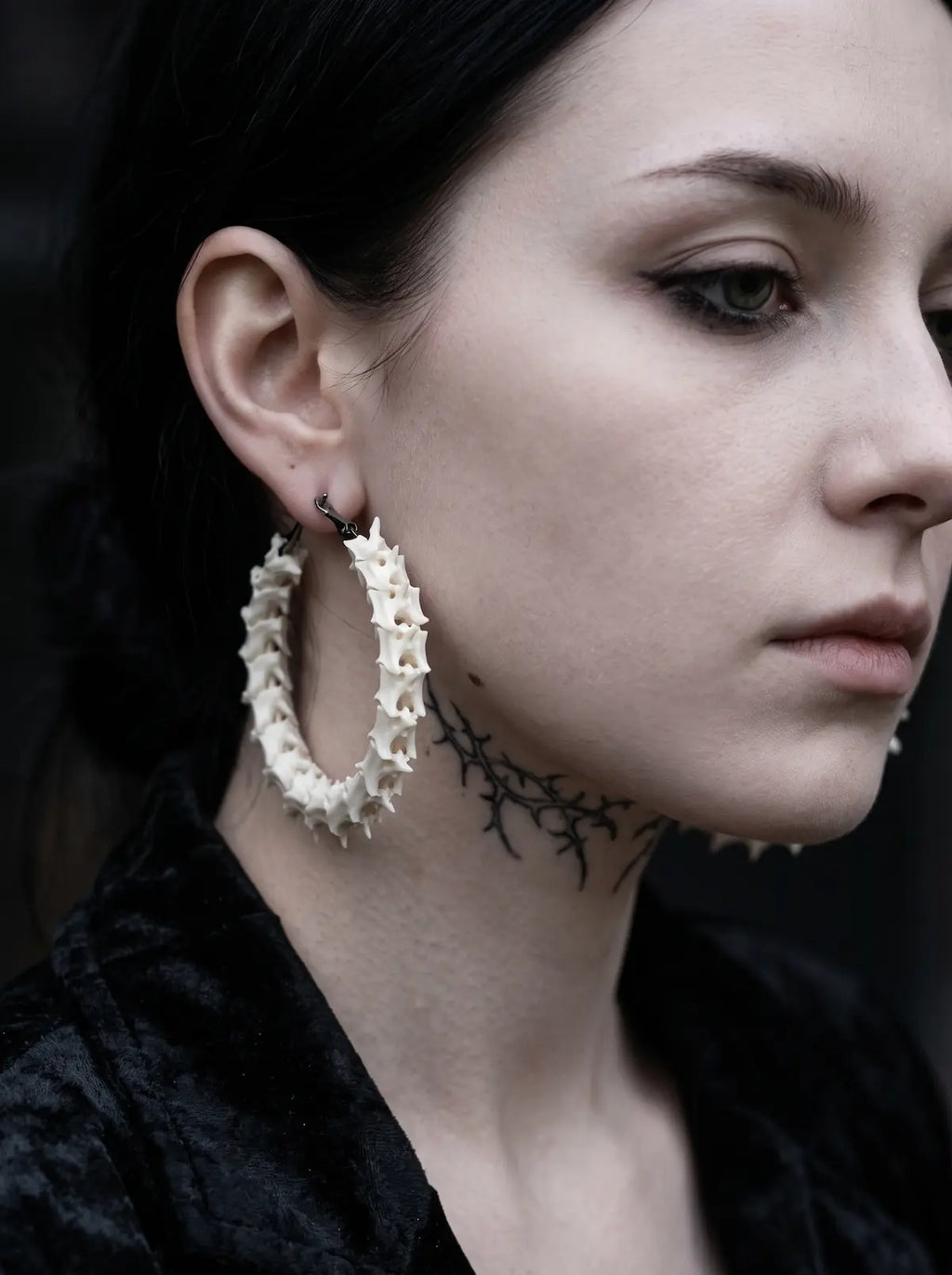 Angled side view of an Ossuary Hoop snake bone earring showing the depth of its curved vertebrae