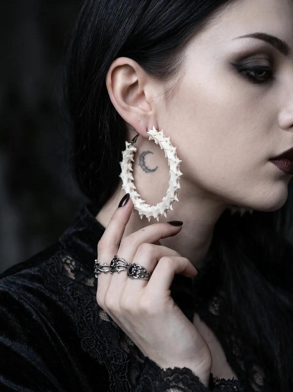 Ossuary Hoop snake bone earring shown with a fingertip beneath the hoop and black lace clothing