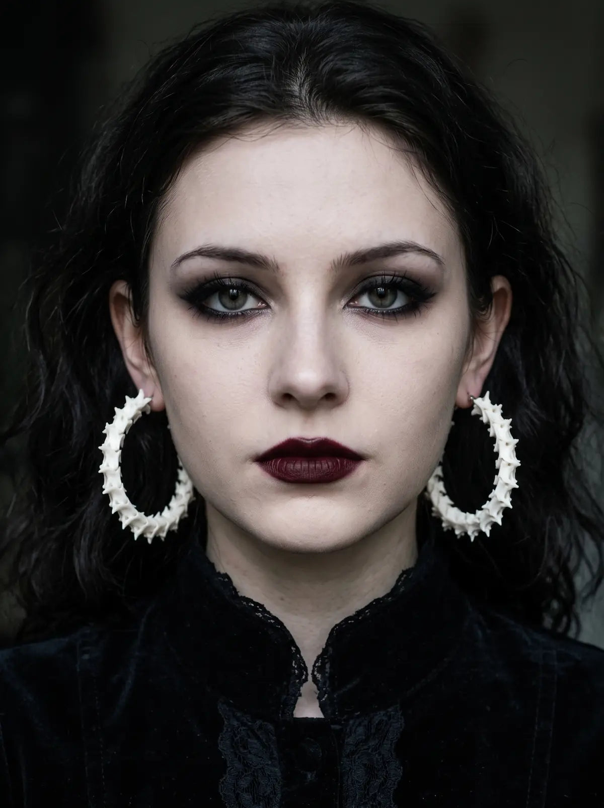 Ossuary Hoop snake bone earrings worn as a pair in a front-facing portrait against a dark background