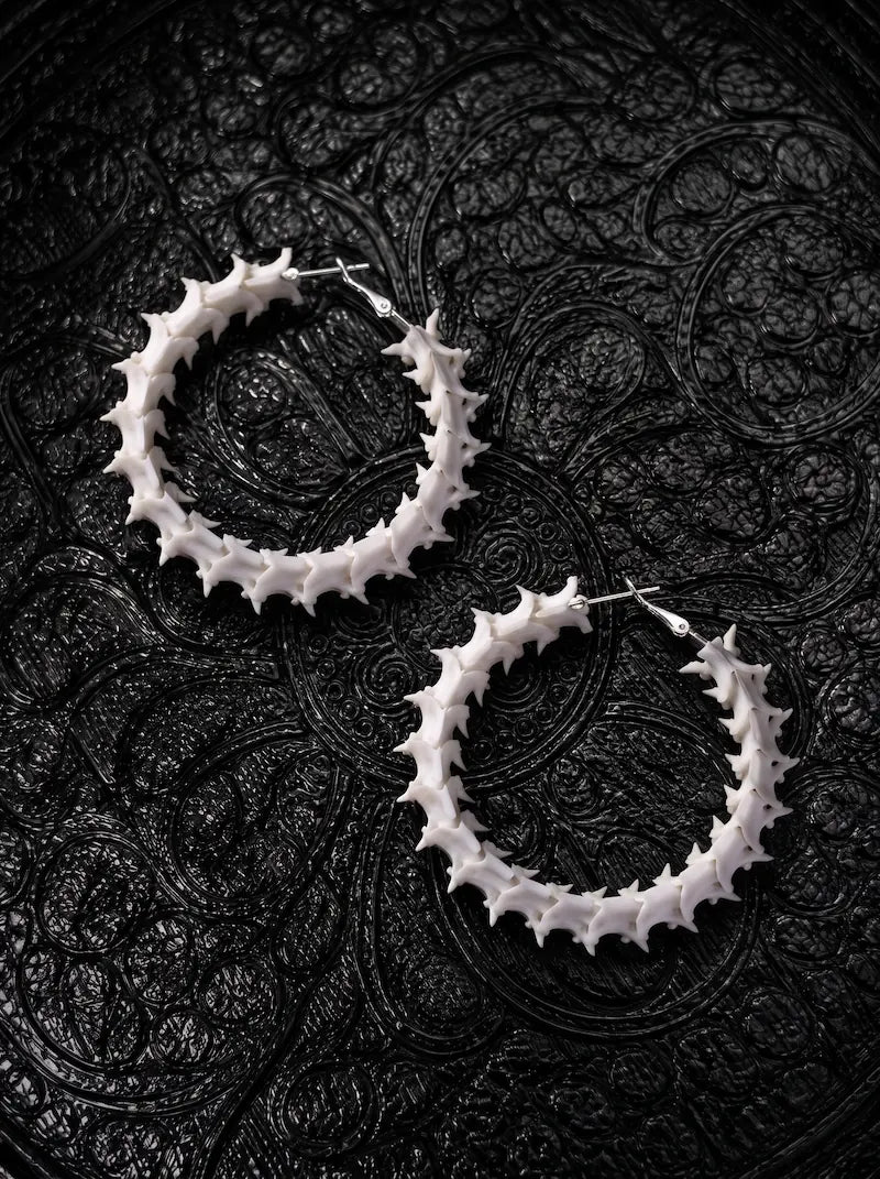 Ossuary Hoop snake bone earrings arranged diagonally as a pair on black patterned fabric