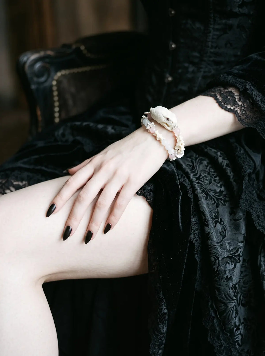 Petalshade Snake Bone Bracelet, pale bone bracelet with pink bead details worn on a wrist above a black skirt