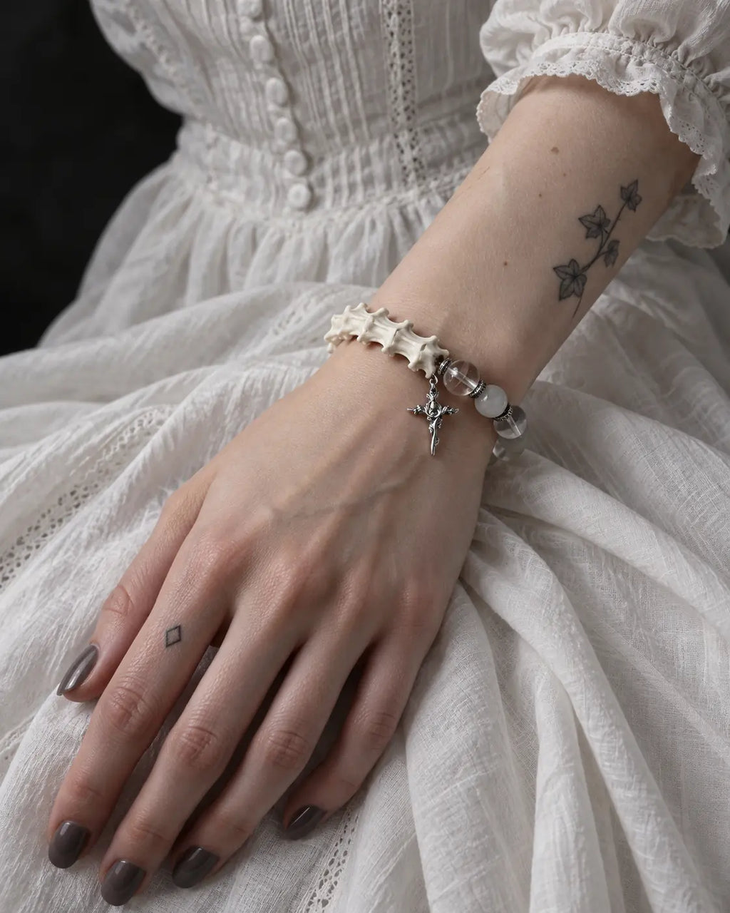 Phantom Rose snake bone bracelet on a hand resting on a white lace skirt, with its cross hanging below