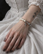 Phantom Rose snake bone bracelet on a hand resting on a white lace skirt, with its cross hanging below