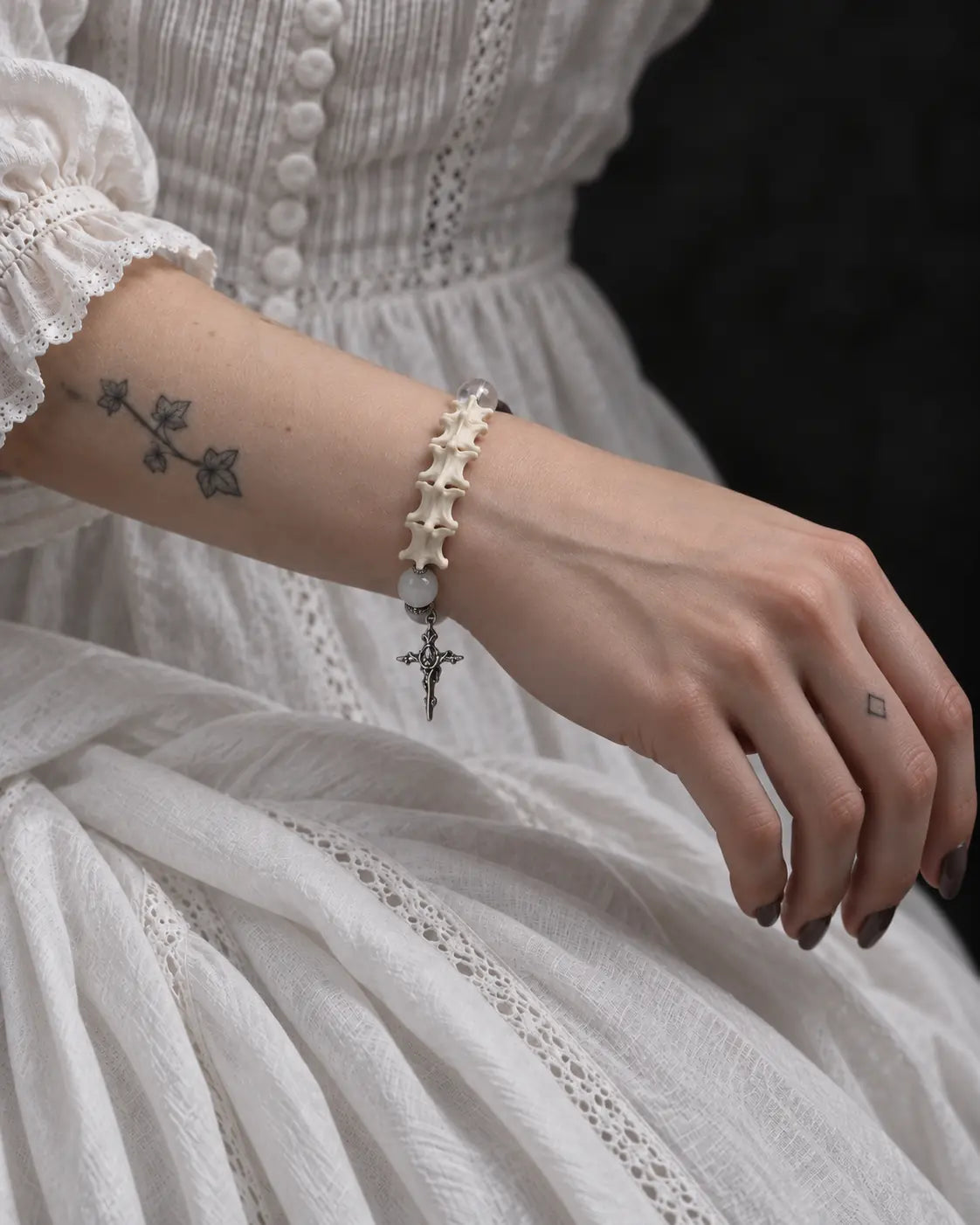 Side view of the Phantom Rose snake bone bracelet worn above a white lace cuff, showing the hanging cross