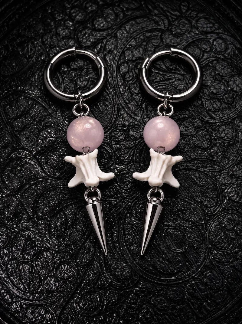 Prismatic Fang snake bone earrings with soft pink beads and polished silver-tone spikes on black patterned fabric