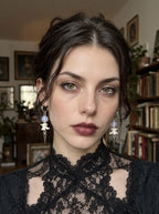 Violet-bead Prismatic Fang snake bone earrings worn as a pair above a black lace collar