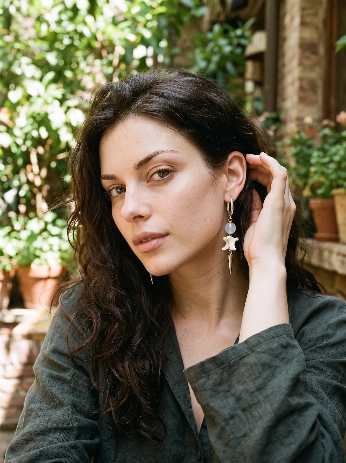 Prismatic Fang snake bone earring with a pale blue bead, worn outdoors with the hair tucked back