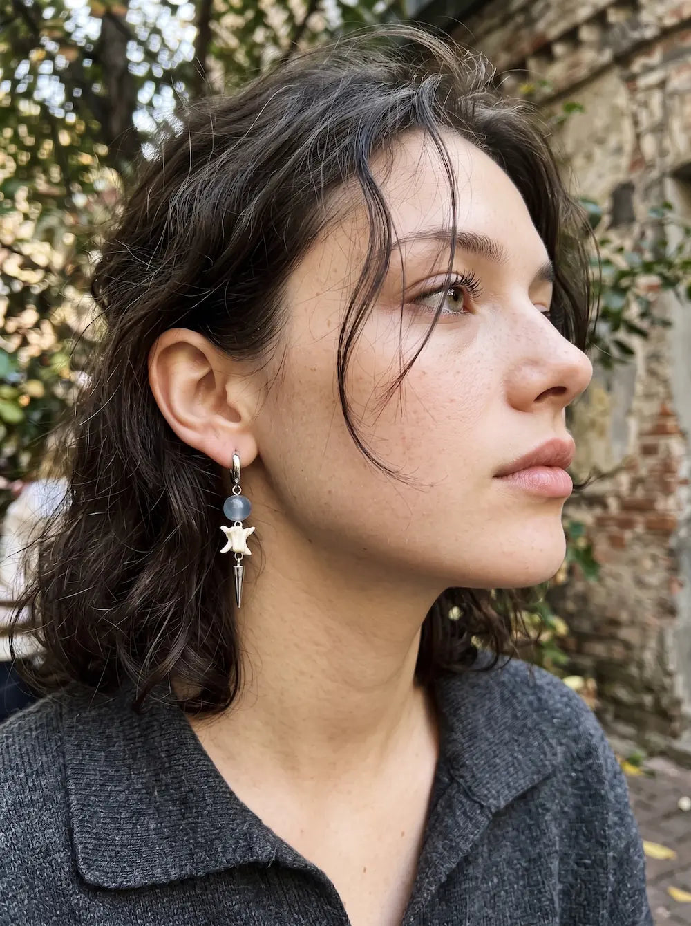Blue-bead Prismatic Fang snake bone earring shown in an outdoor side profile above a dark collar