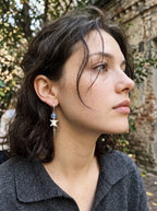 Blue-bead Prismatic Fang snake bone earring shown in an outdoor side profile above a dark collar