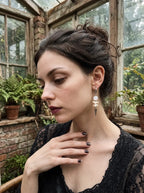 Prismatic Fang snake bone earring with a pale bead and pointed drop, worn beside pinned-up hair