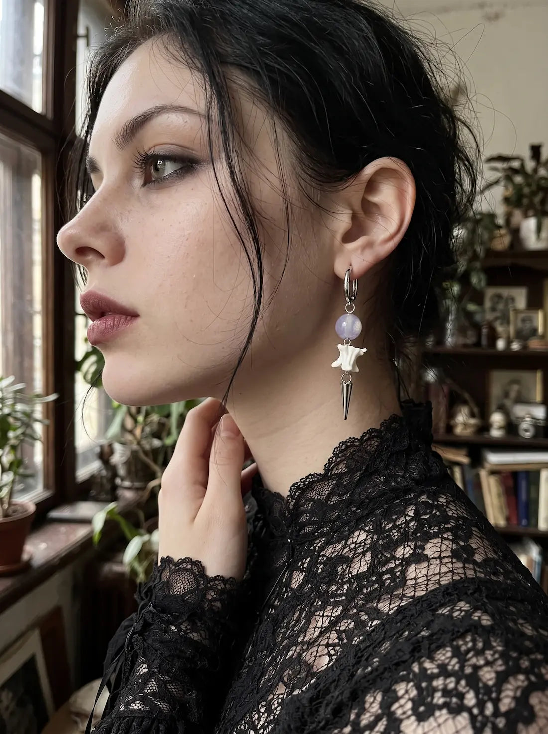 Violet-bead Prismatic Fang snake bone earring shown in close side profile with a hand at the neck