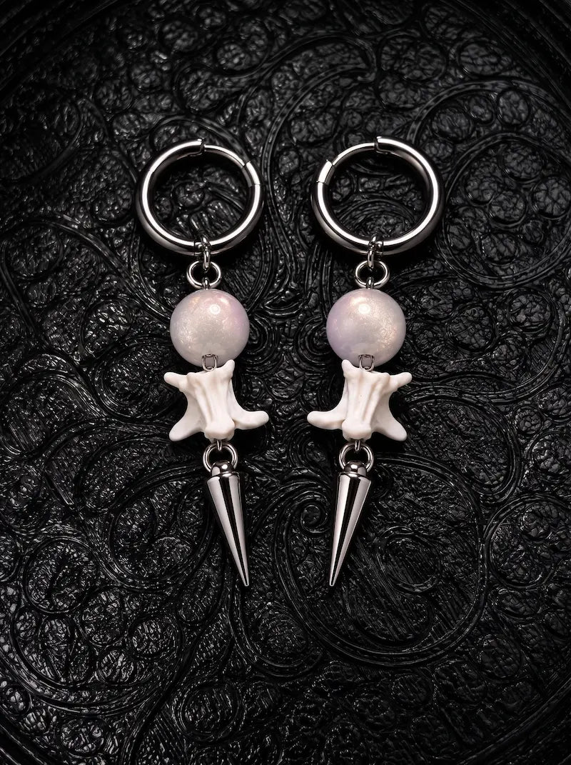 Prismatic Fang snake bone earrings with pale blush-gray beads and silver-tone spikes on black patterned fabric