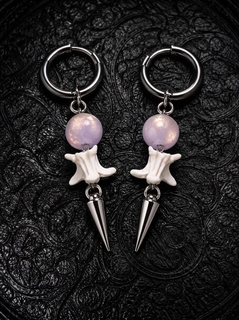 Prismatic Fang snake bone earrings with pale lavender beads and polished silver-tone spikes on black patterned fabric