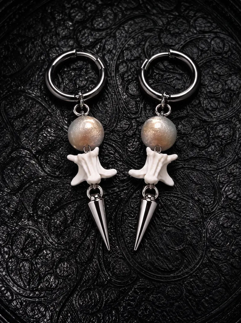 Prismatic Fang snake bone earrings with warm brown beads and polished silver-tone spikes on black patterned fabric