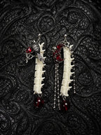 Ravenmoon Snake Bone Earrings, pair of pale vertebrae drop earrings with dark red beads and metal chains on black fabric