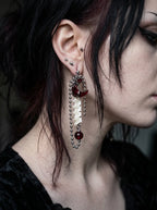 Ravenmoon Snake Bone Earrings, long bone earring worn at the ear, showing red bead and chain accents from the side