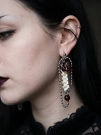 Ravenmoon Snake Bone Earrings, close view of Ravenmoon earring showing its pale spine motif and chain tassels