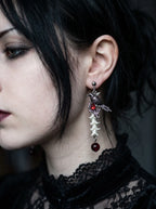 Ravenmoon Snake Bone Earrings, bone-and-red-bead earring hanging beside dark hair in a close side portrait