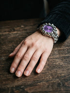Razorclaw Gothic Watch, purple-dial metal watch on a wrist resting against a dark wood surface
