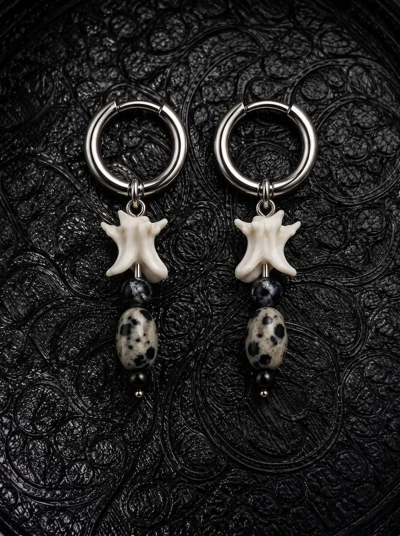 Relicstone snake bone earrings with black beads and oval speckled stones beneath silver-tone hoops on black fabric