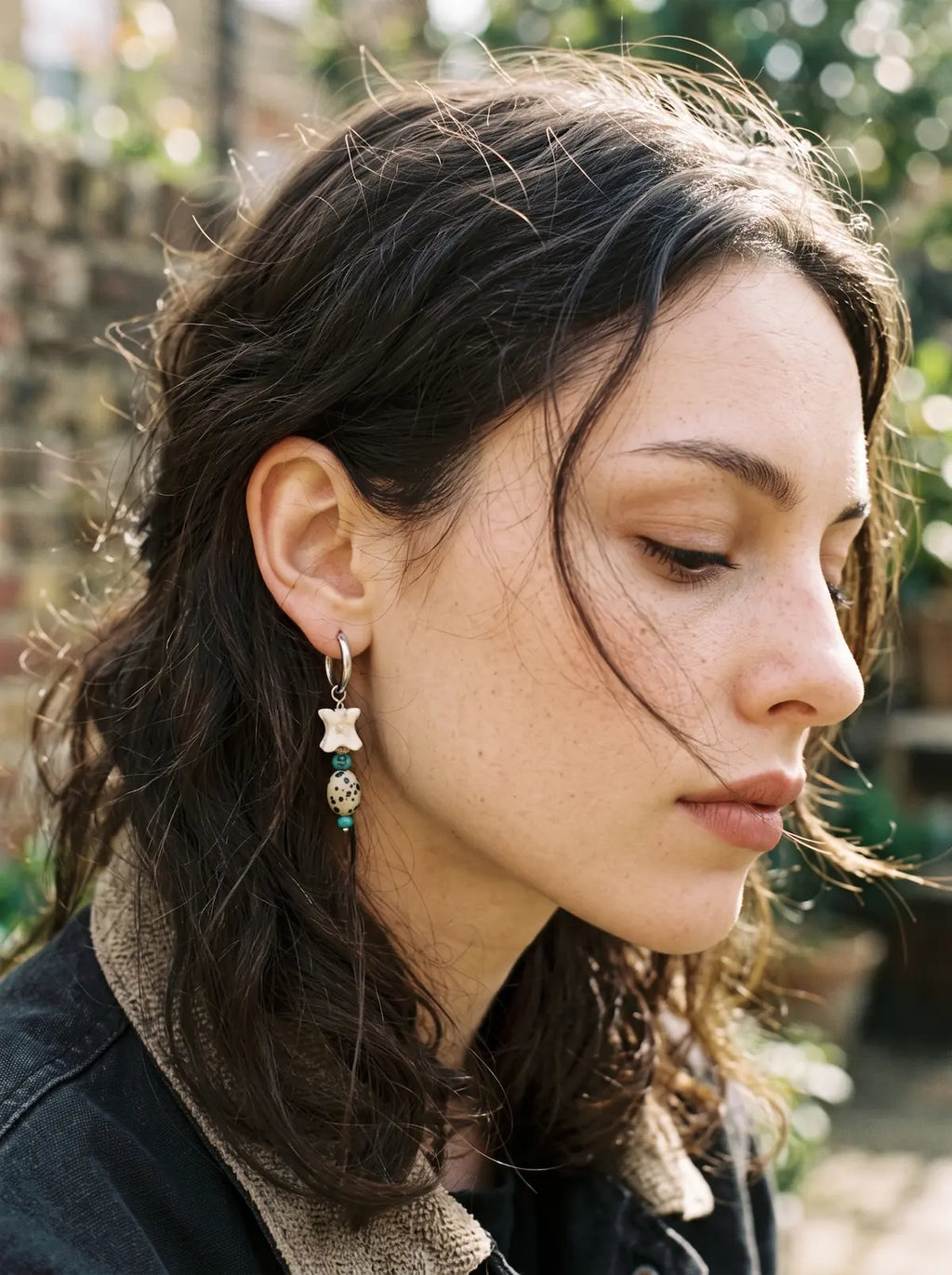 Blue-green Relicstone snake bone earring worn in a close side view outdoors