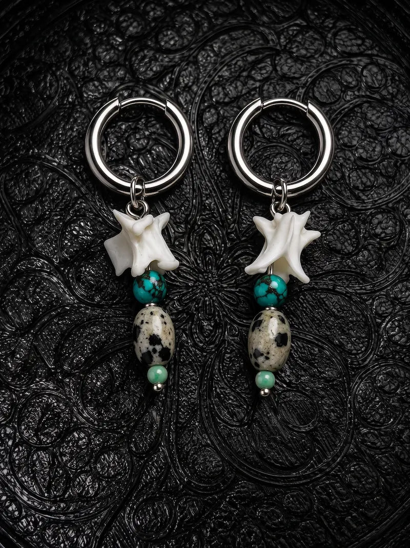 Relicstone snake bone earrings with turquoise-colored beads and oval speckled stones on black patterned fabric