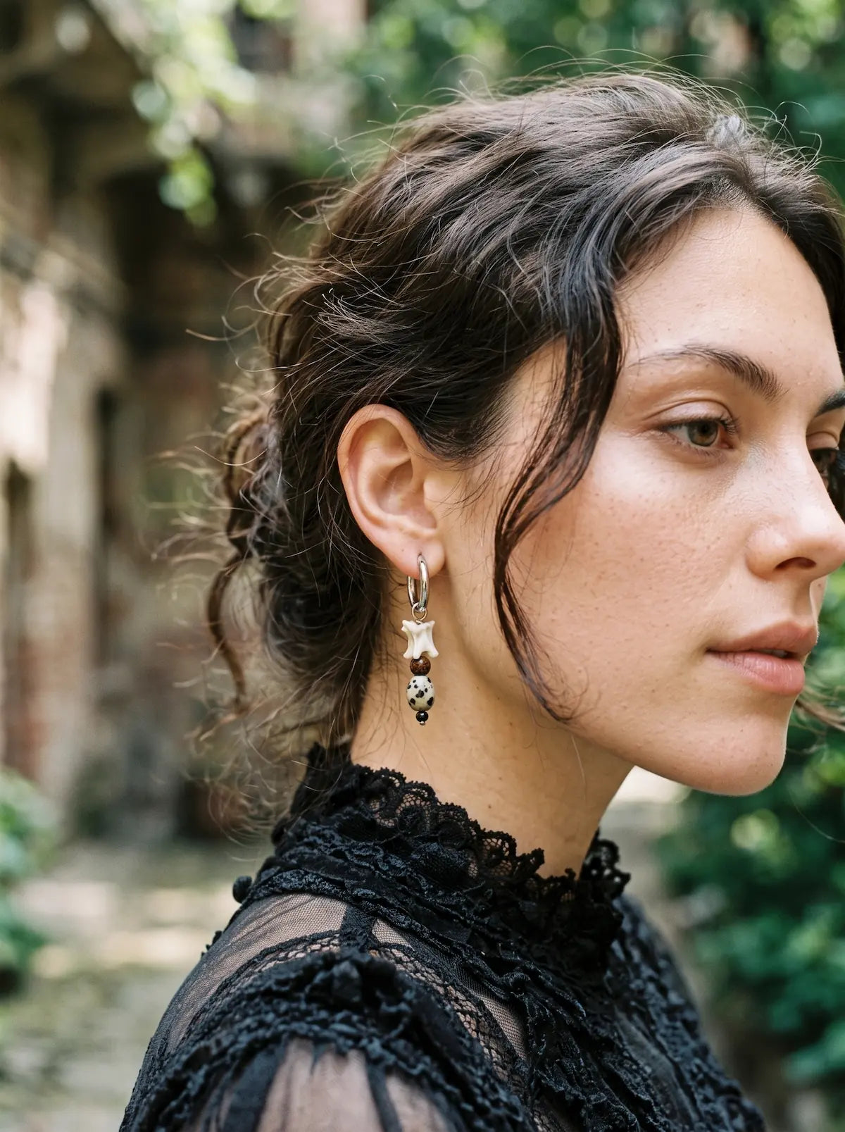 Side view of a dark Relicstone snake bone earring worn above a black lace collar