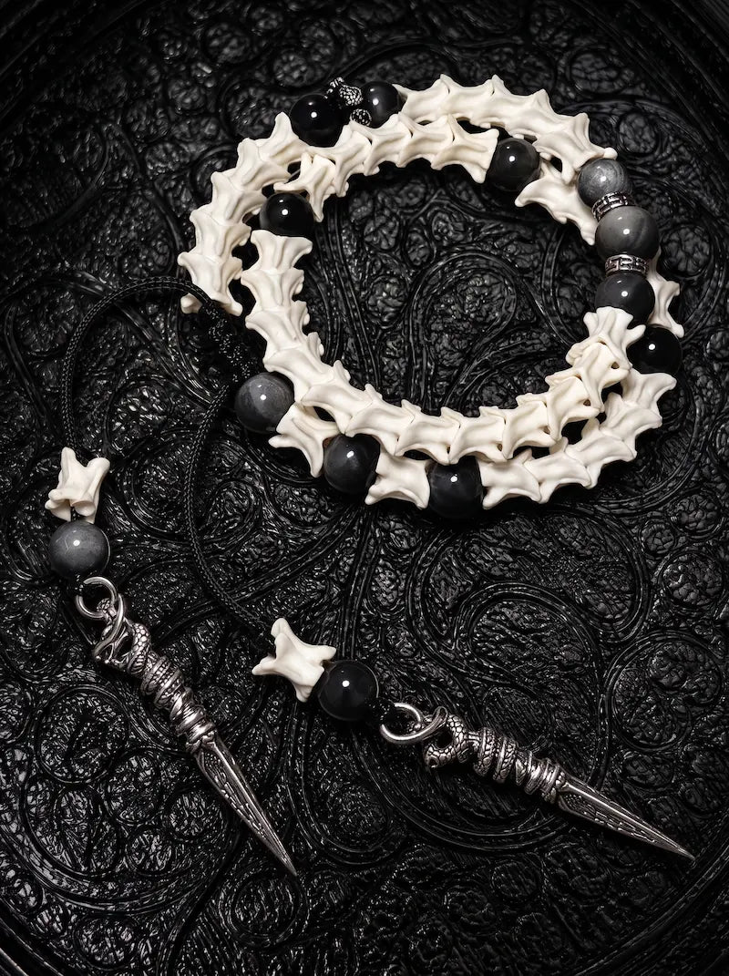 Ritual Spear double-wrap snake bone bracelet with black and gray beads and two long pointed metal drops on black fabric