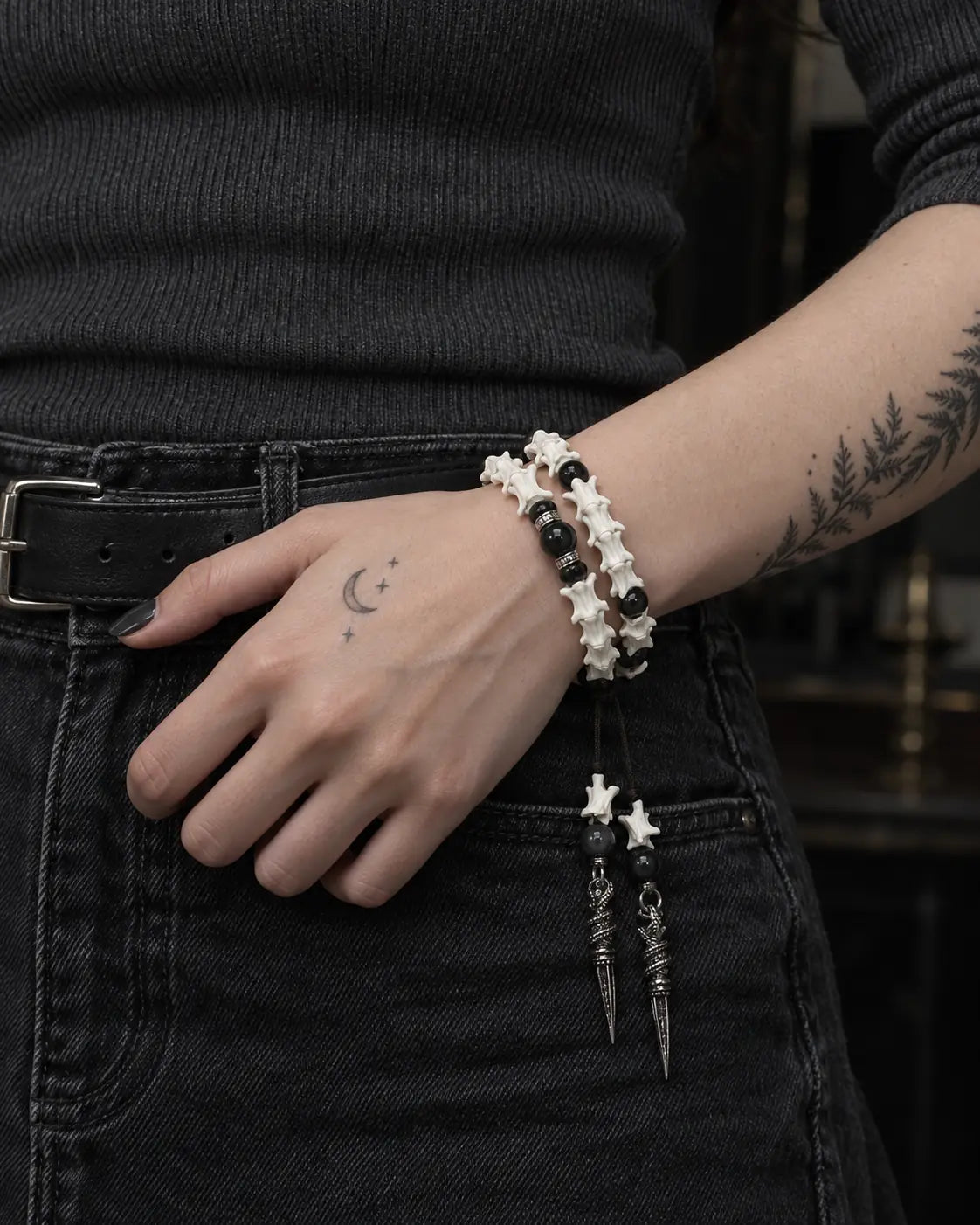 Ritual Spear snake bone bracelet worn with the hand resting beside a black belt and jeans