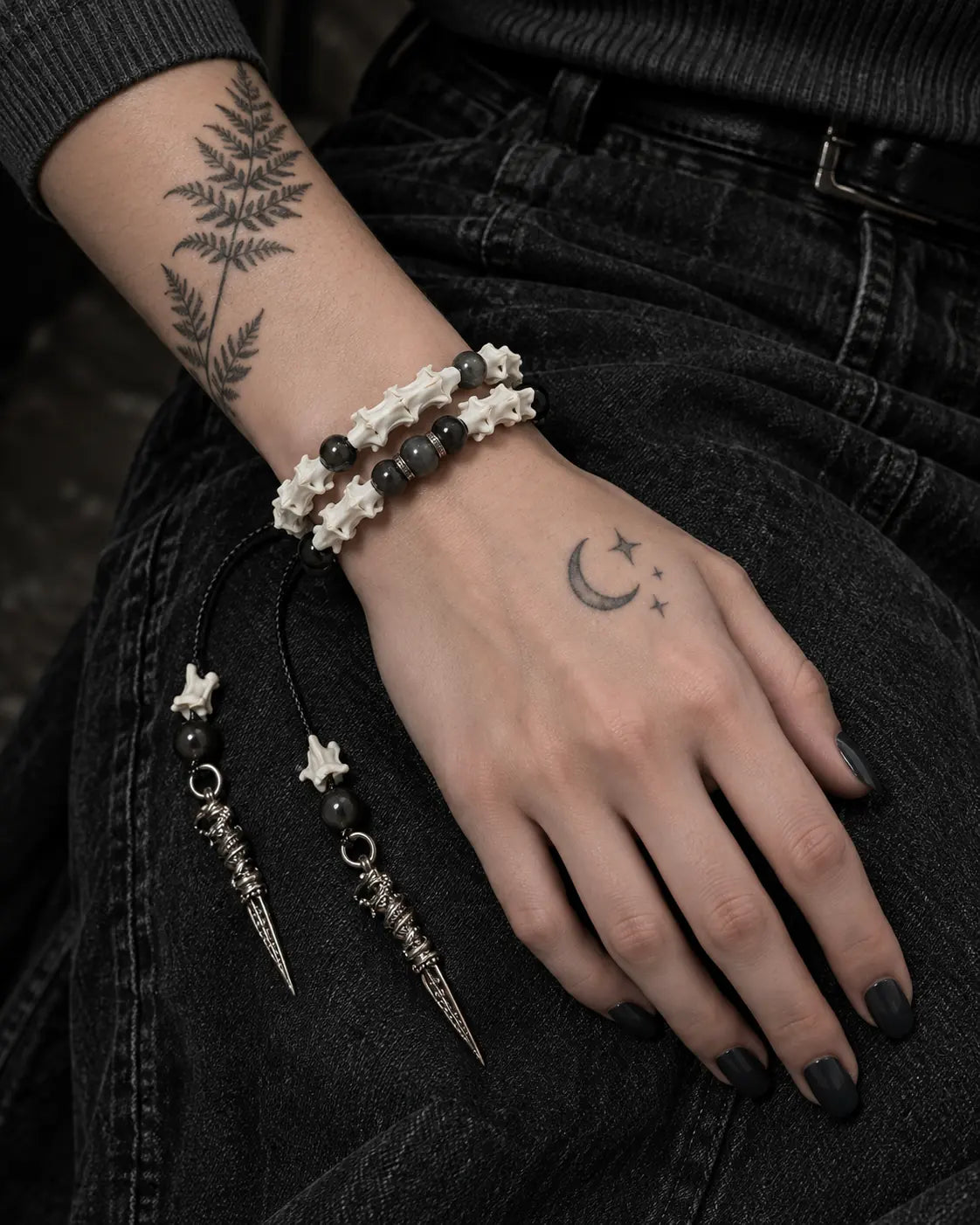 Ritual Spear snake bone bracelet on a hand resting on the thigh, with both pointed drops against black denim
