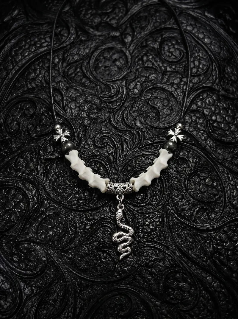 Sablecoil Snake Bone Necklace, white vertebrae necklace with black bead accents and a coiled metal snake pendant