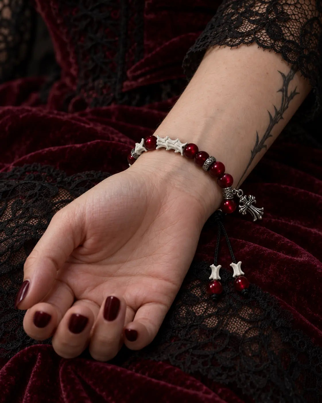 Palm-up view of the Scarlet Cross snake bone bracelet showing red beads, its cross charm and hanging cord ends