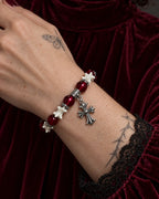Close-up of the Scarlet Cross snake bone bracelet showing its silver-tone cross and red beads against burgundy velvet