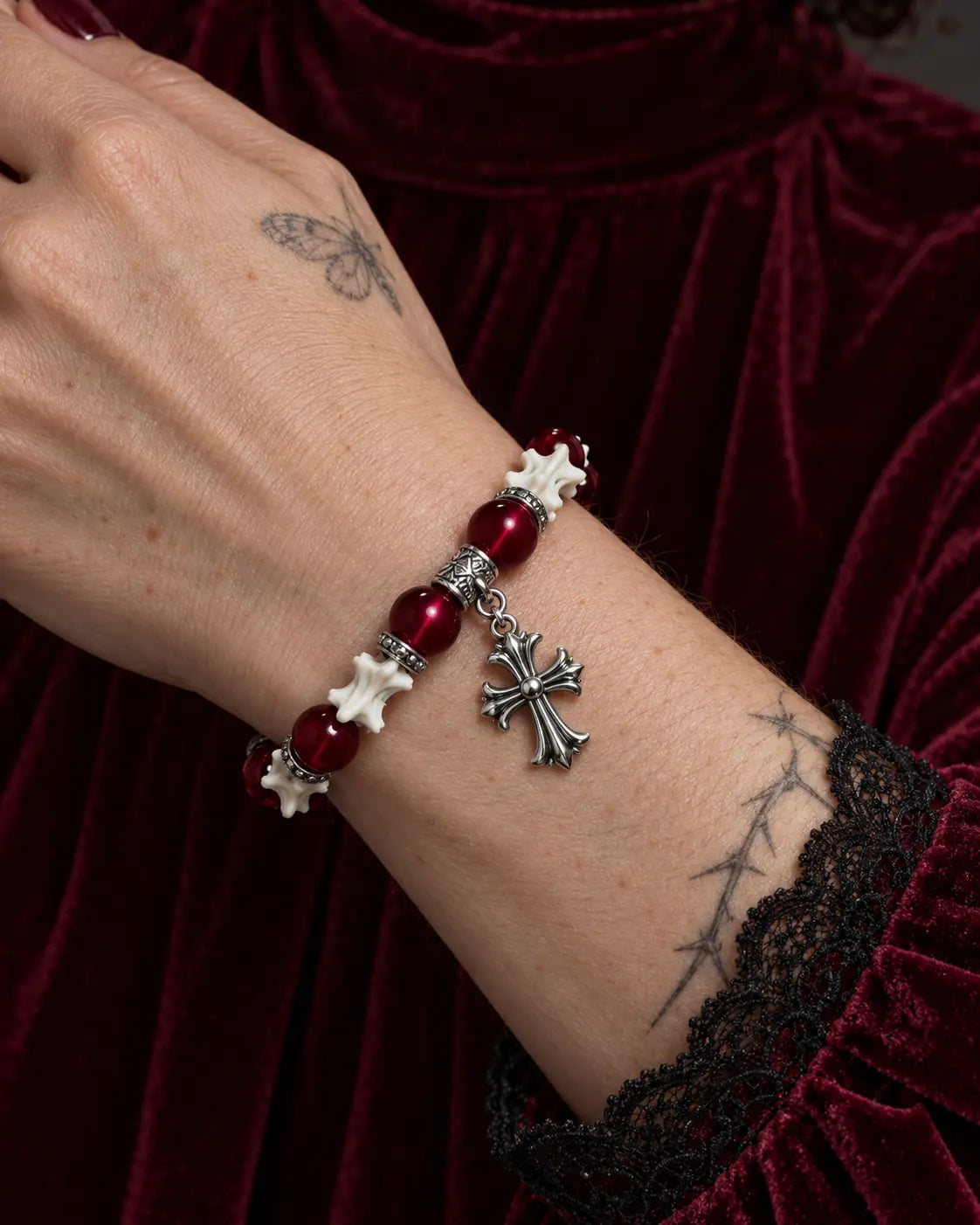 Close-up of the Scarlet Cross snake bone bracelet showing its silver-tone cross and red beads against burgundy velvet