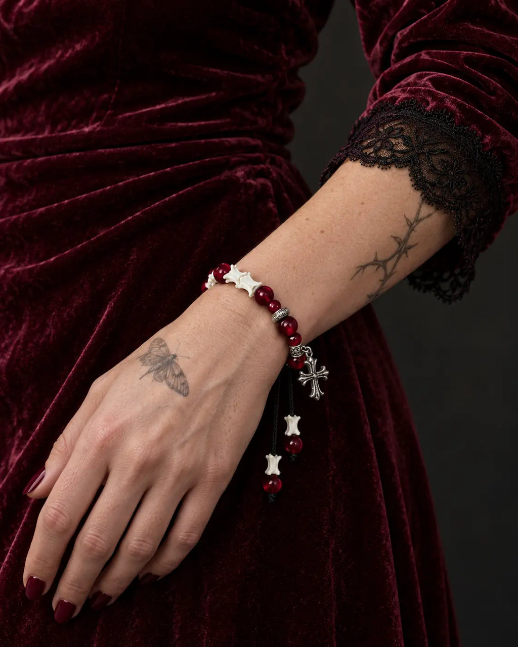 Scarlet Cross snake bone bracelet on a hand resting against a burgundy velvet skirt beside a black lace cuff