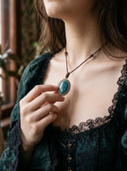 Teal Serpent Relic snakeskin pendant held between the fingers at the chest