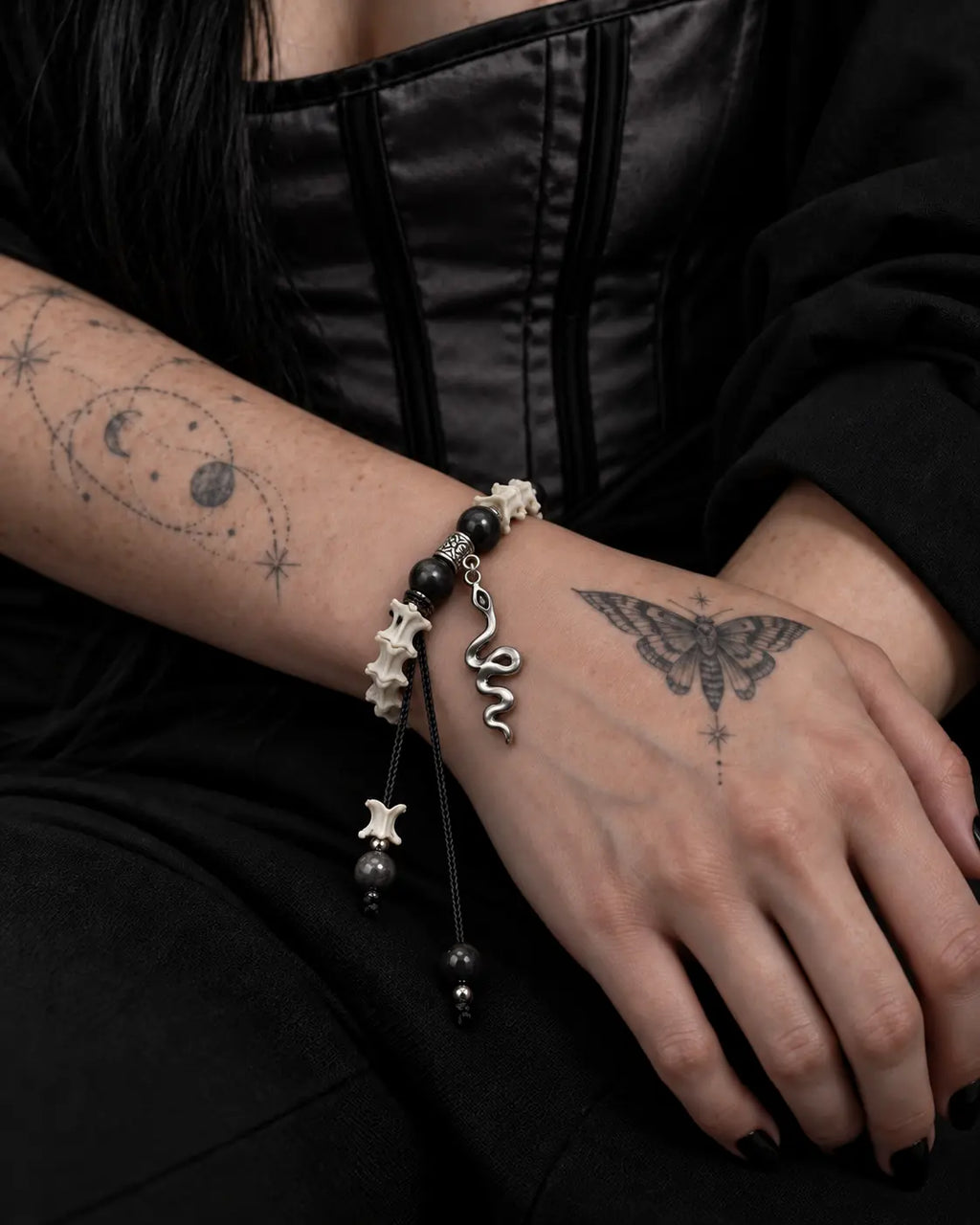 Shadow Serpent snake bone bracelet worn with the hand resting across the lap below a black corset