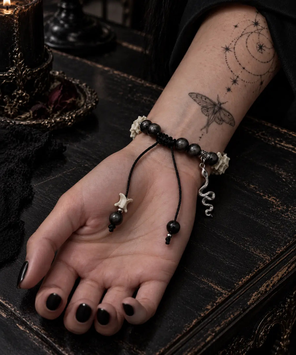 Palm-up view of the Shadow Serpent snake bone bracelet on a wooden table, showing black cords and its snake charm