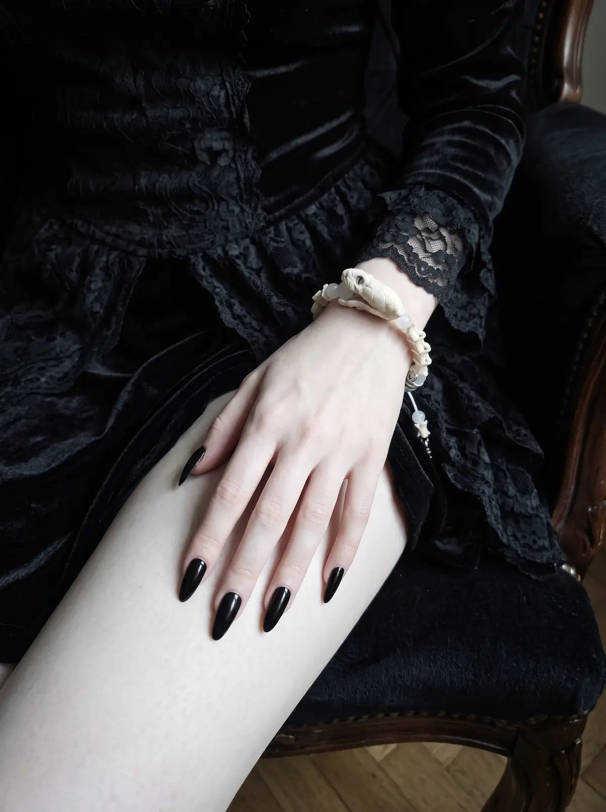 Silver Omen Snake Bone Bracelet, white vertebrae bracelet on a hand resting over a black skirt