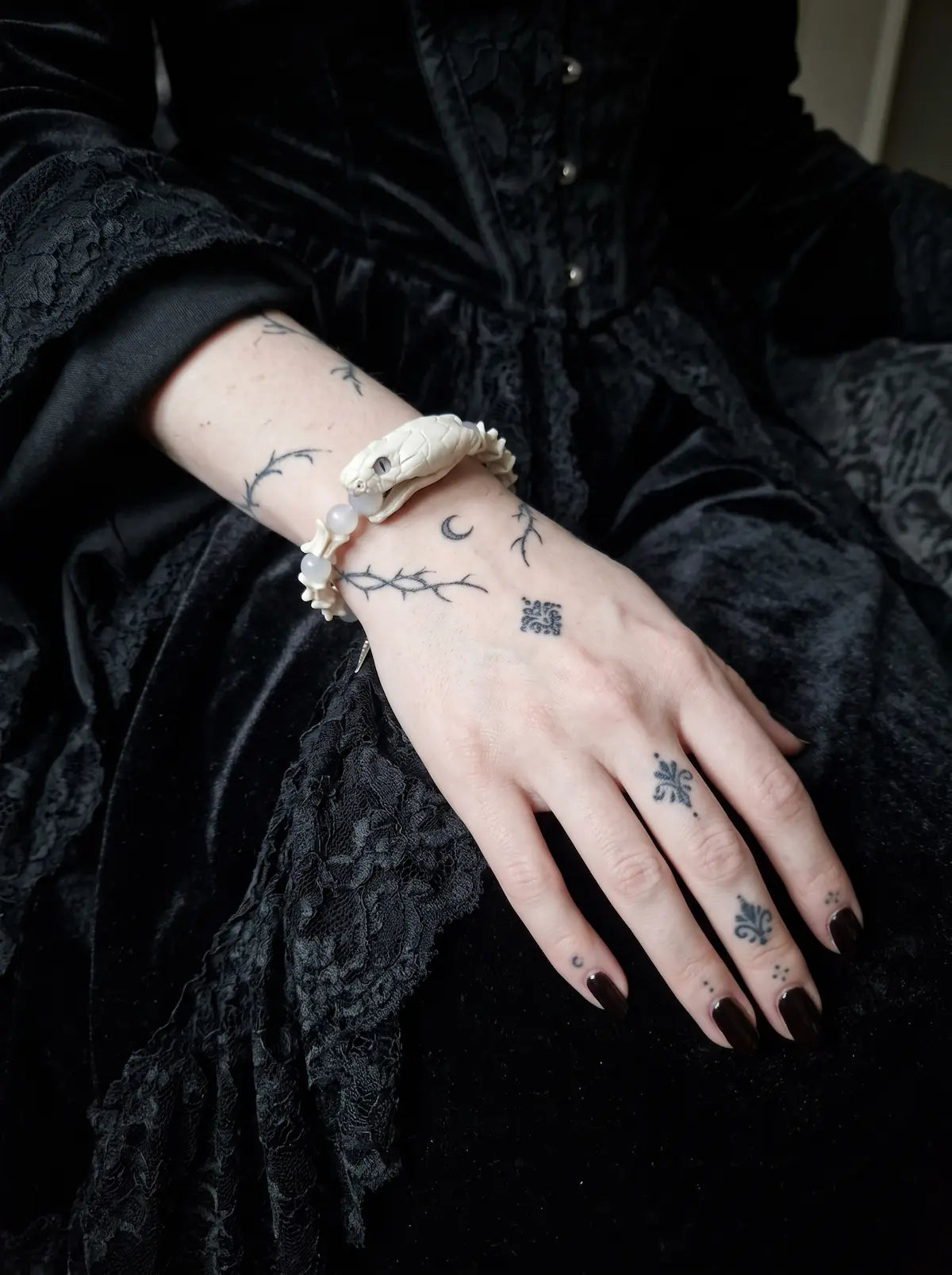 Silver Omen Snake Bone Bracelet, white snake bone bracelet with dangling silver-tone charms over black sleeves